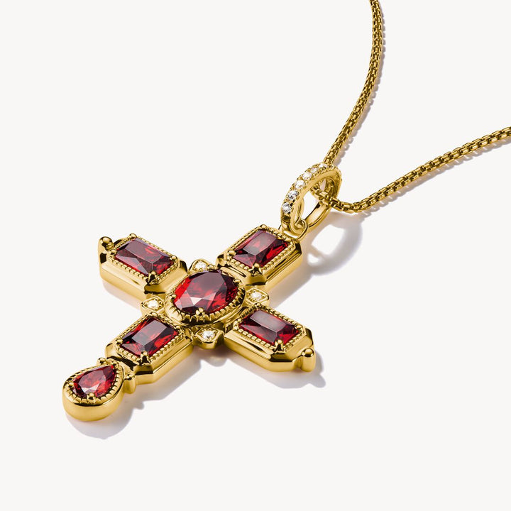 Gold cross pendant with red gemstones on a white background