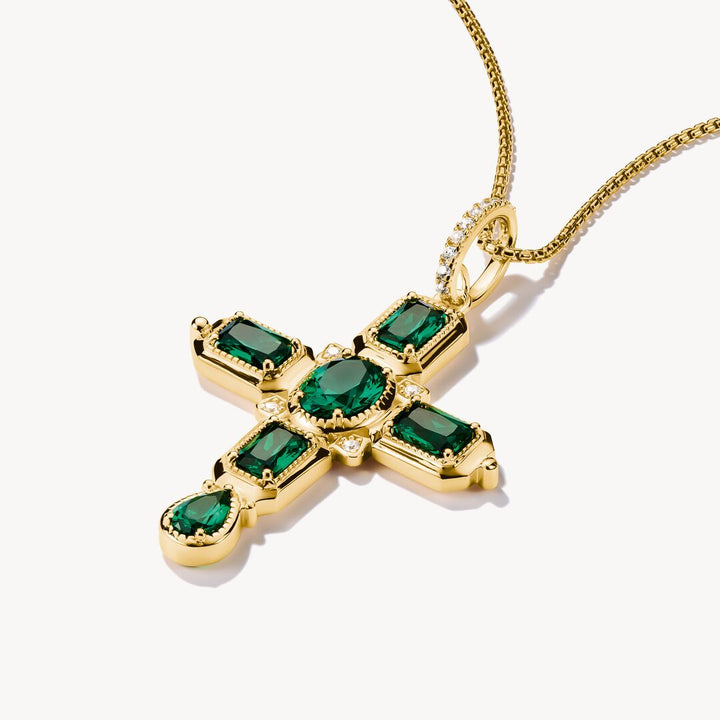Gold cross pendant with green gemstones on a white background