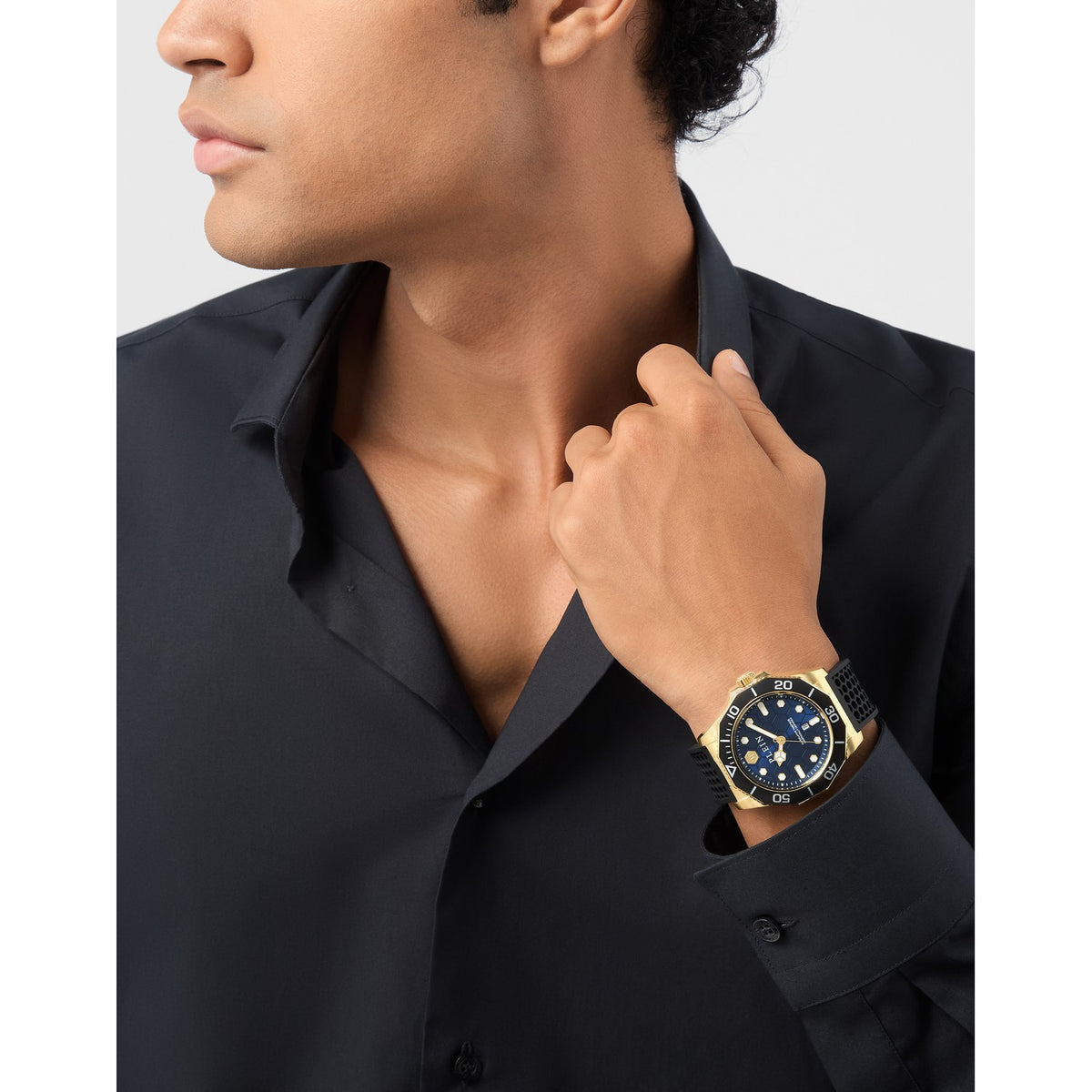 Man wearing a black shirt with a gold watch on his wrist against a gray background