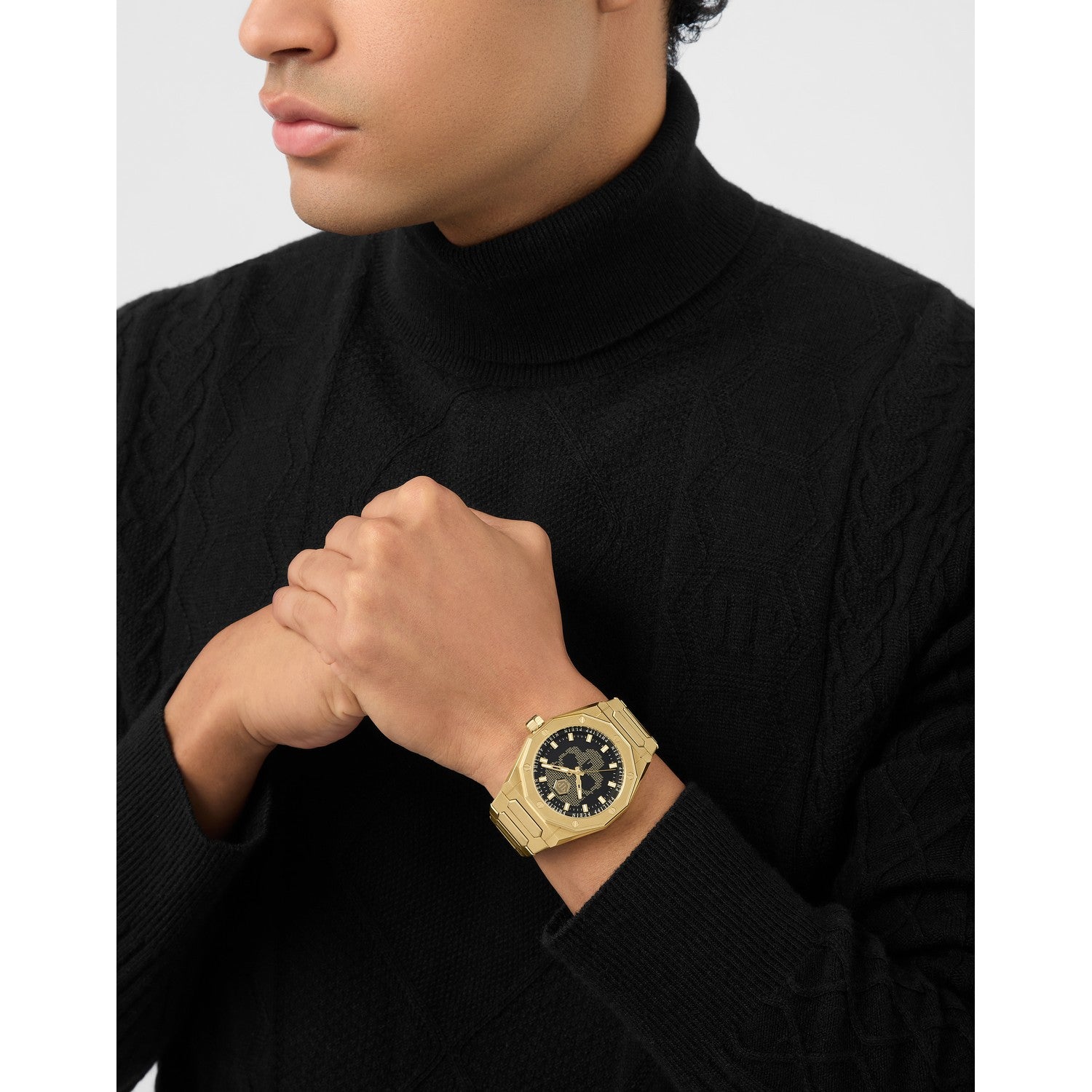 Man wearing a gold watch on his wrist with a plain background