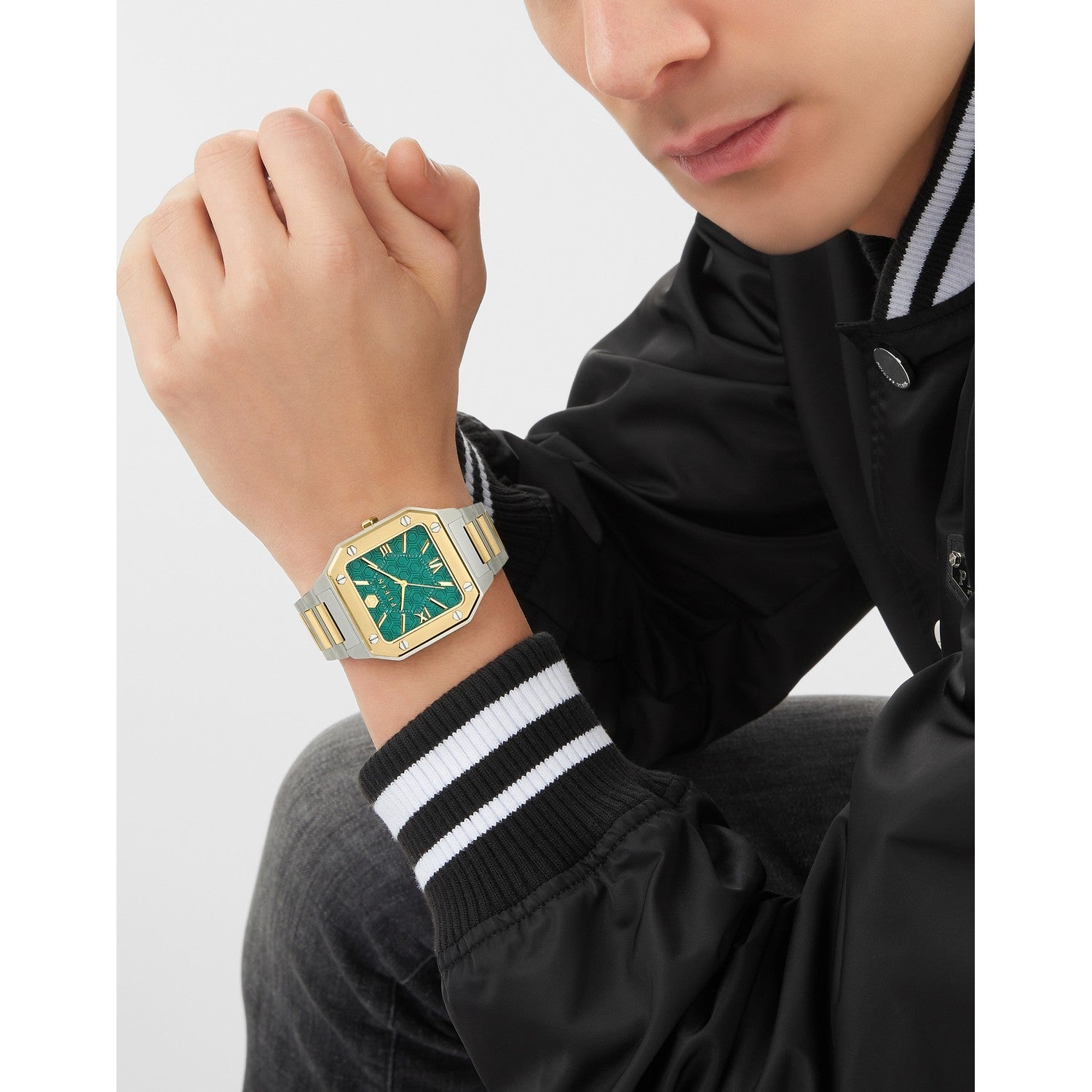 Person wearing a watch with a green face and gold accents on a white background