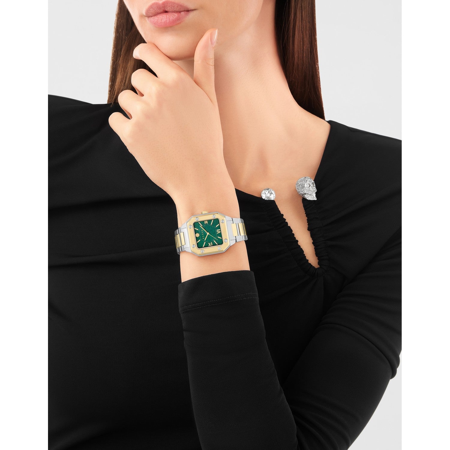Woman wearing a gold watch with a green face and matching bracelet on a plain background