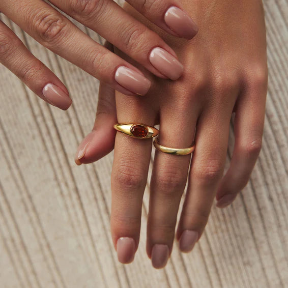 Close-up of a hand wearing two gold rings on a wooden surface