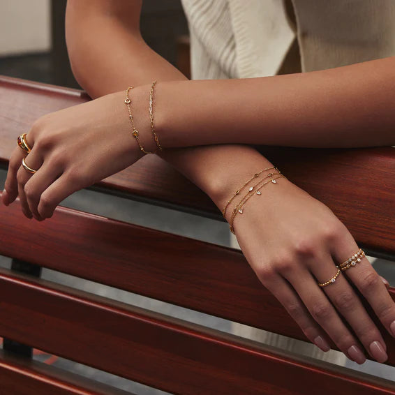 Close-up of a person's hands wearing gold bracelets and rings on a wooden surface.