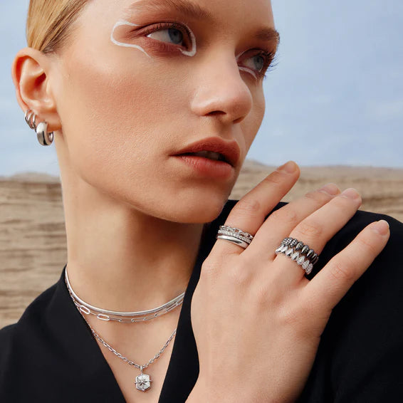 Woman wearing silver jewelry including rings and a necklace against a blurred natural background
