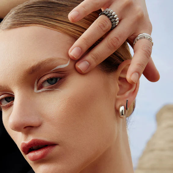 Close-up of a woman's face with a hand touching her hair, wearing earrings and rings.