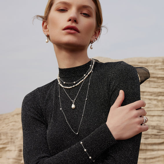 Woman wearing layered necklaces and a ring against a neutral background