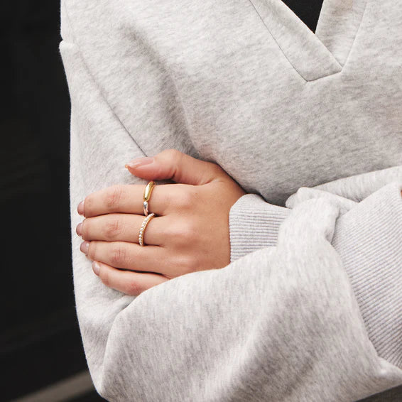 Person wearing a gray sweater with hands clasped together, wearing multiple rings.