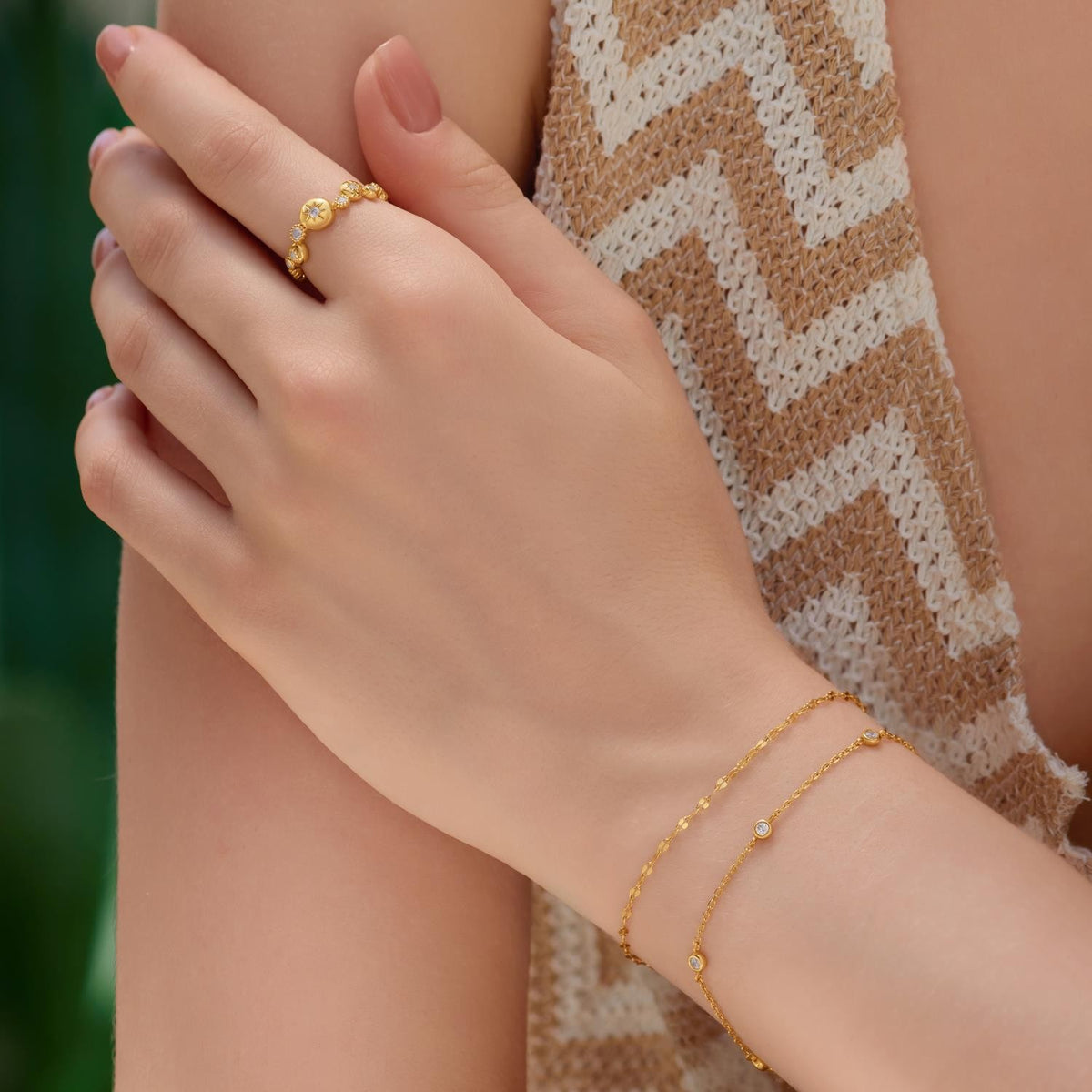 Hand wearing a gold ring and bracelet with a blurred background