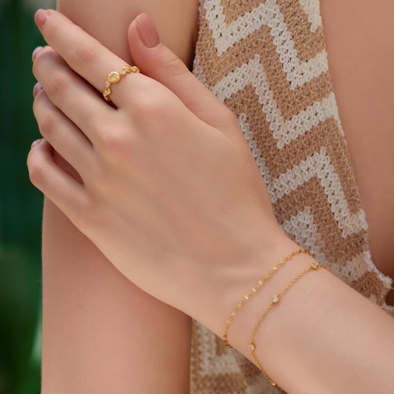 Hand wearing a gold ring and bracelet with a blurred background