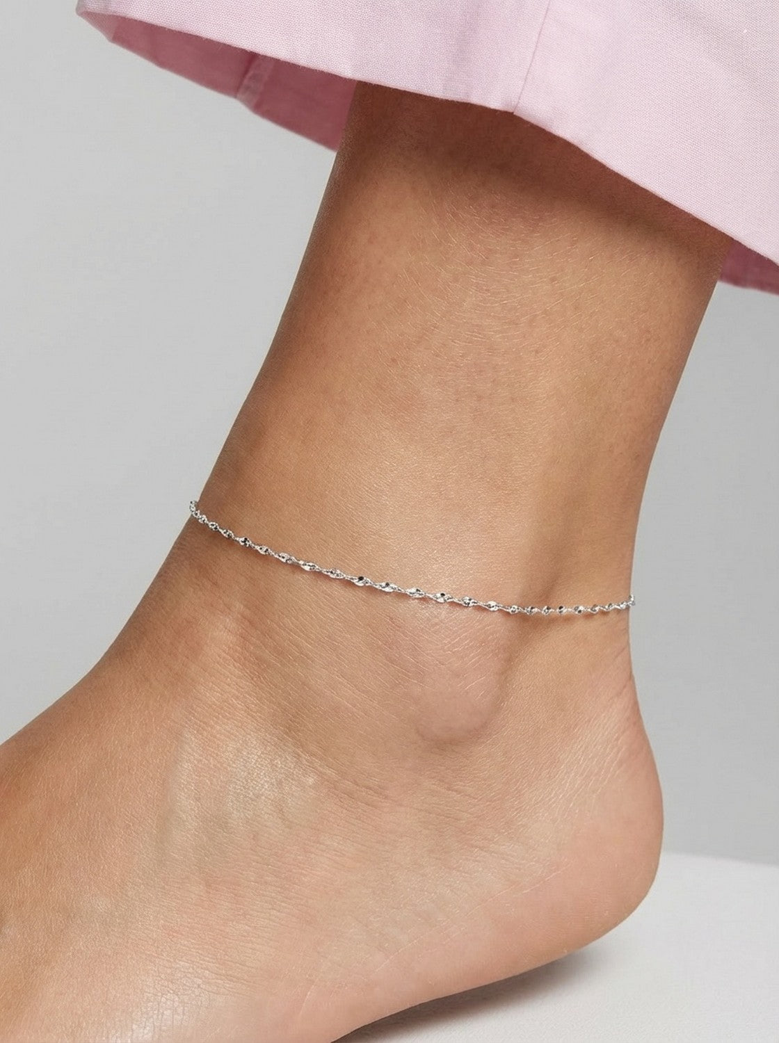 Silver anklet on a person's ankle against a neutral background