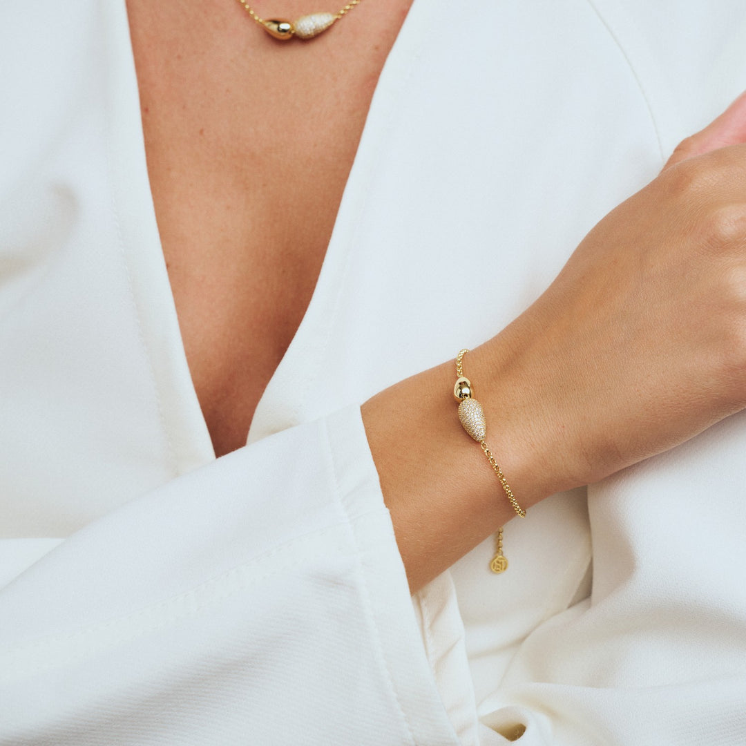 Gold bracelet on a wrist with a white fabric background