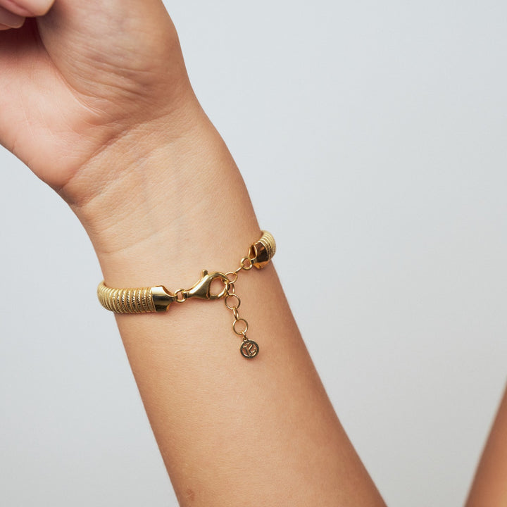 Gold bracelet on a wrist against a light gray background