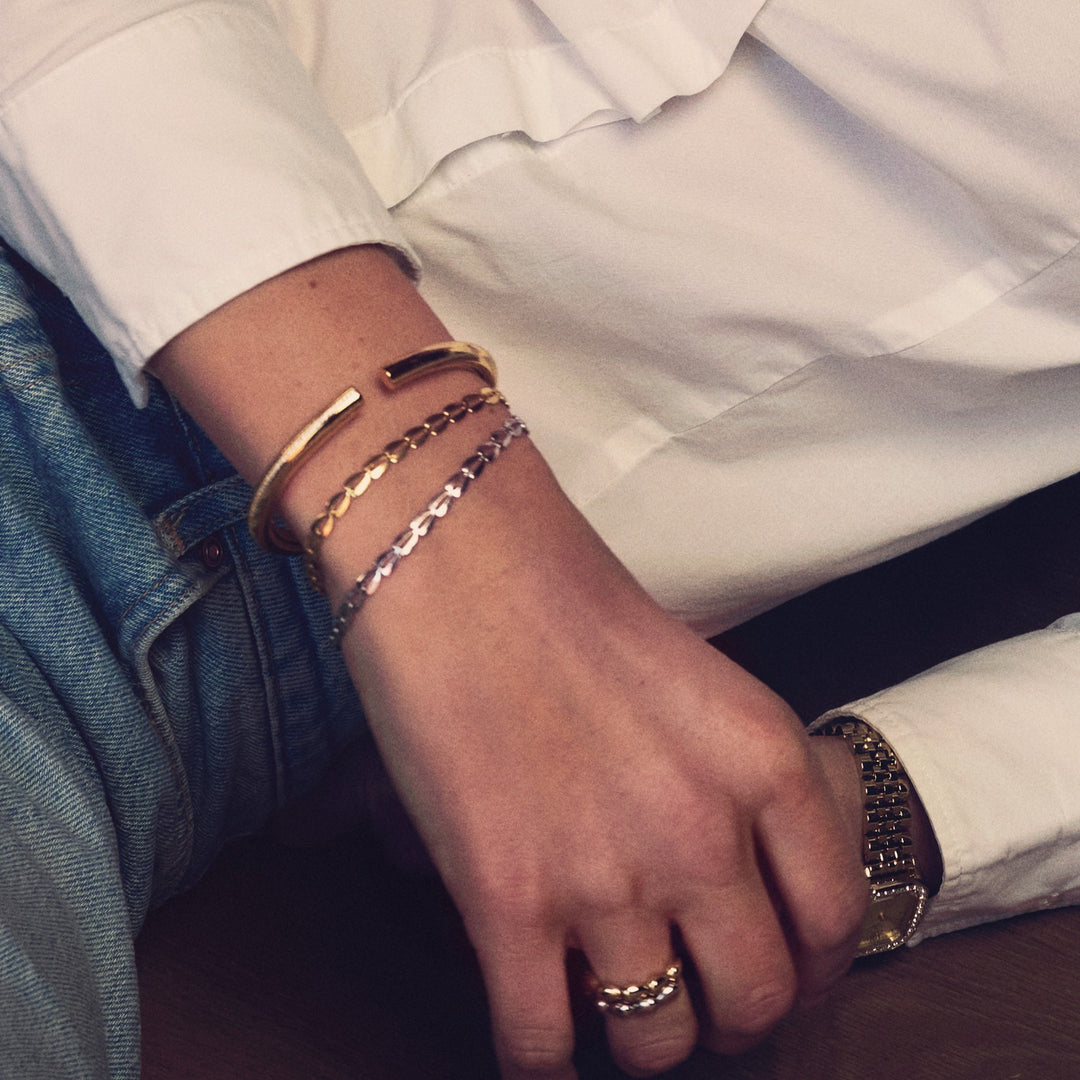 Hand wearing multiple bracelets on a white shirt background