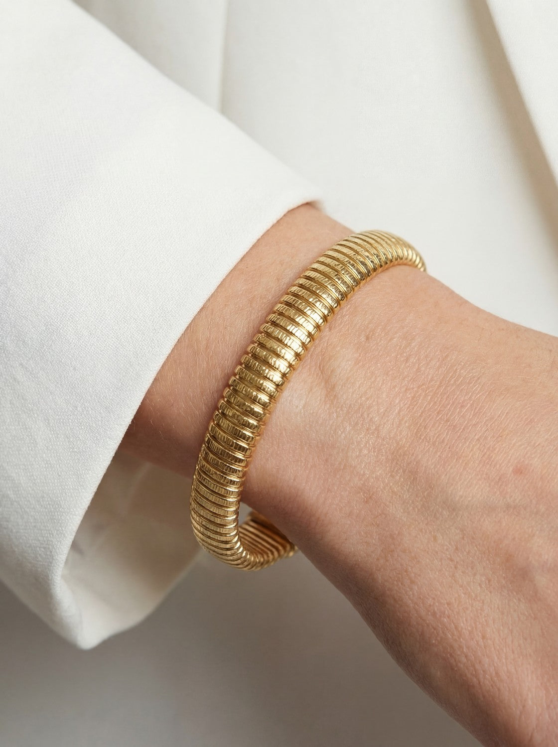 Gold bracelet on a person's wrist with a white sleeve.