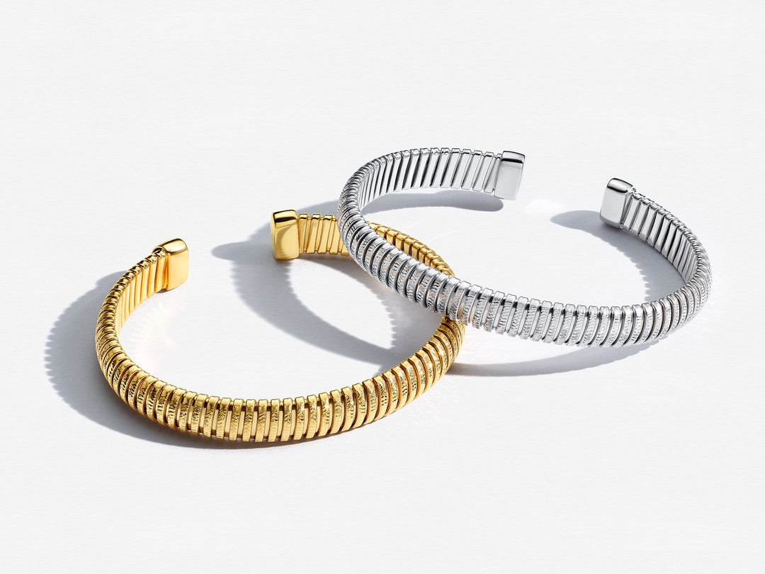 Two bracelets, one gold and one silver, on a white background
