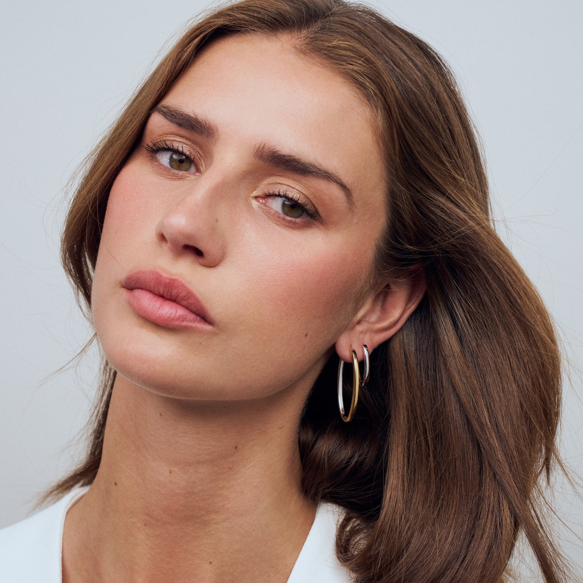 Woman wearing gold hoop earrings against a plain background