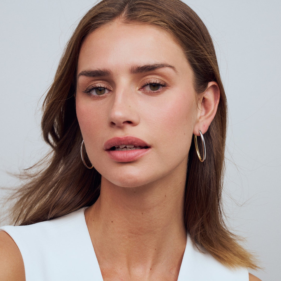 Woman wearing gold hoop earrings against a plain background