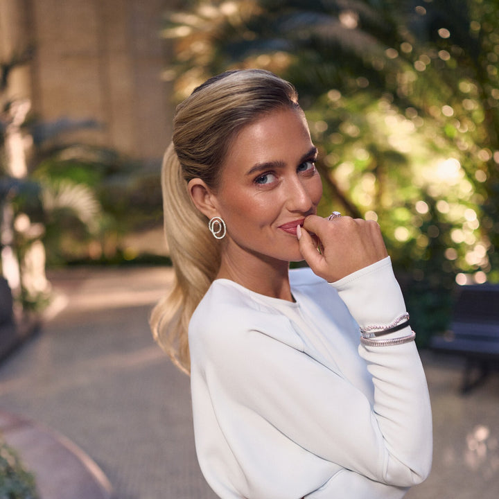 Woman in a white outfit standing outdoors with greenery in the background