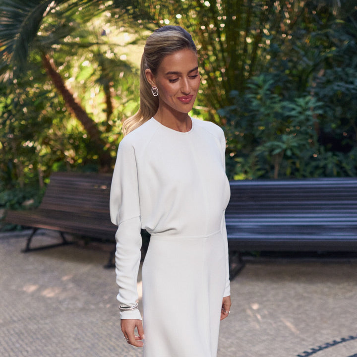 Woman in a white dress standing outdoors with greenery in the background