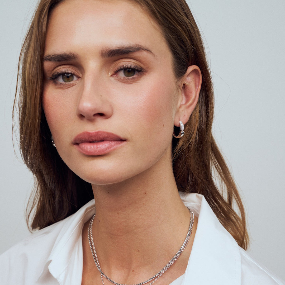 Close-up of a woman wearing a silver necklace and earrings against a plain background