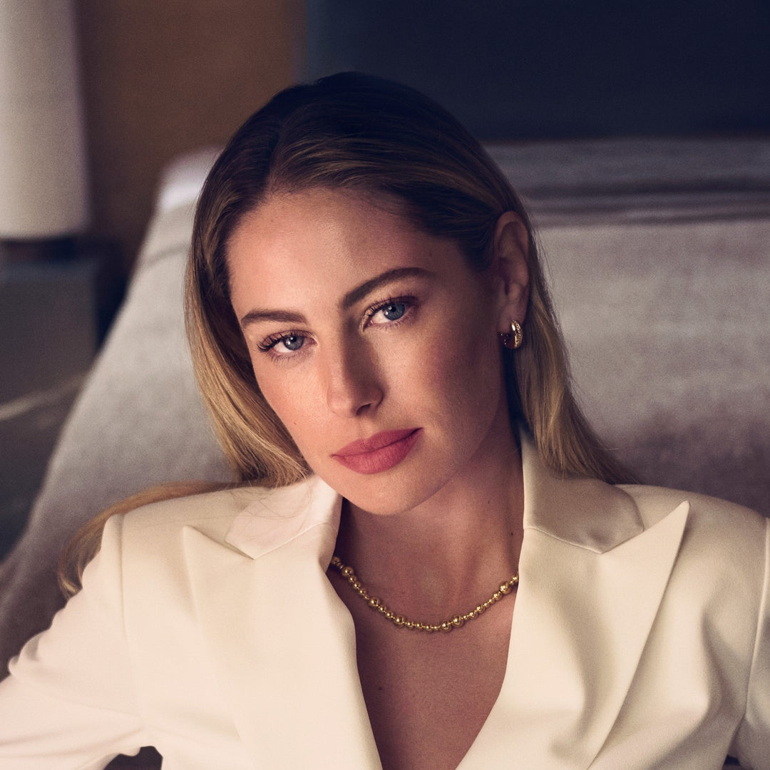 Woman wearing a white blazer and gold necklace in an indoor setting