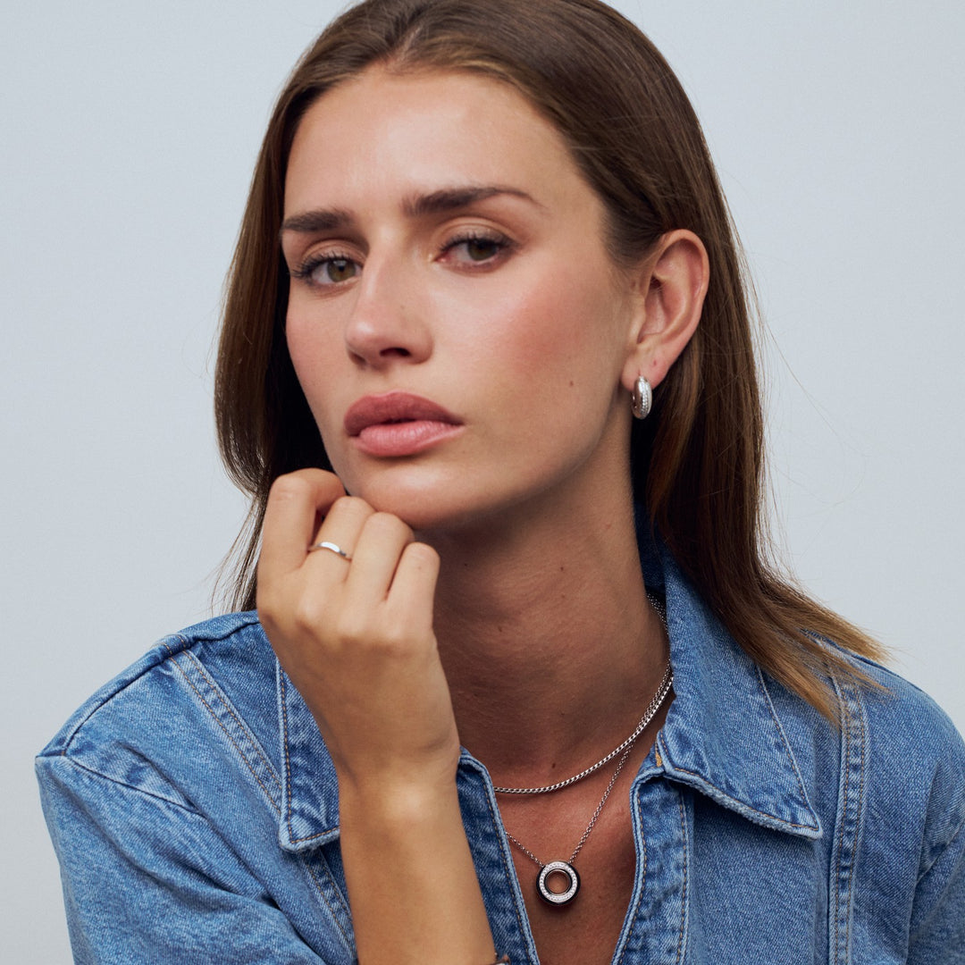 Woman wearing a denim jacket with jewelry against a plain background