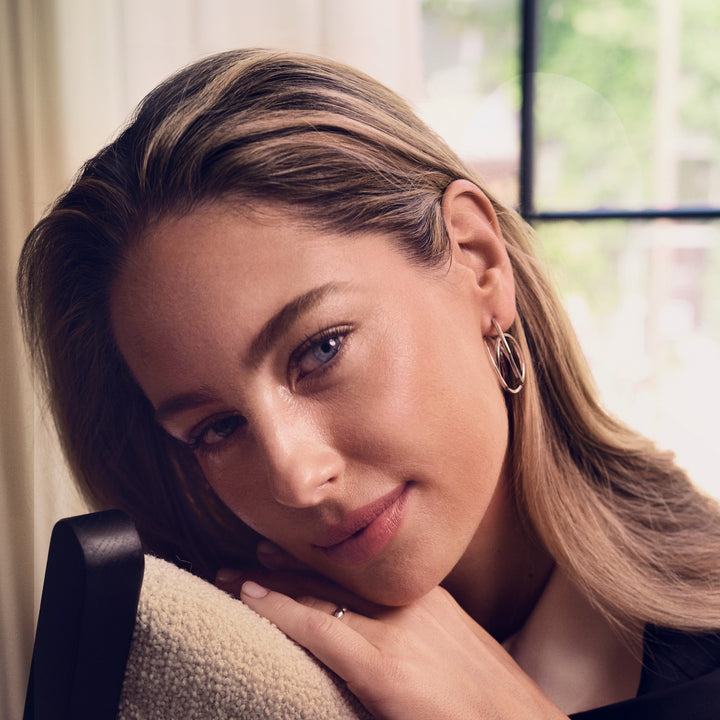 Woman with blonde hair and hoop earrings sitting indoors.
