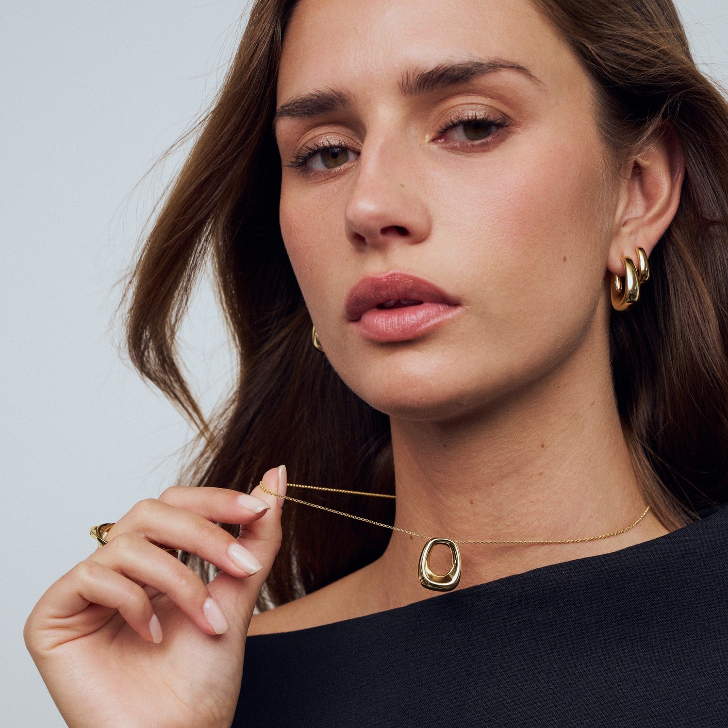 Woman wearing a gold necklace and hoop earrings against a neutral background
