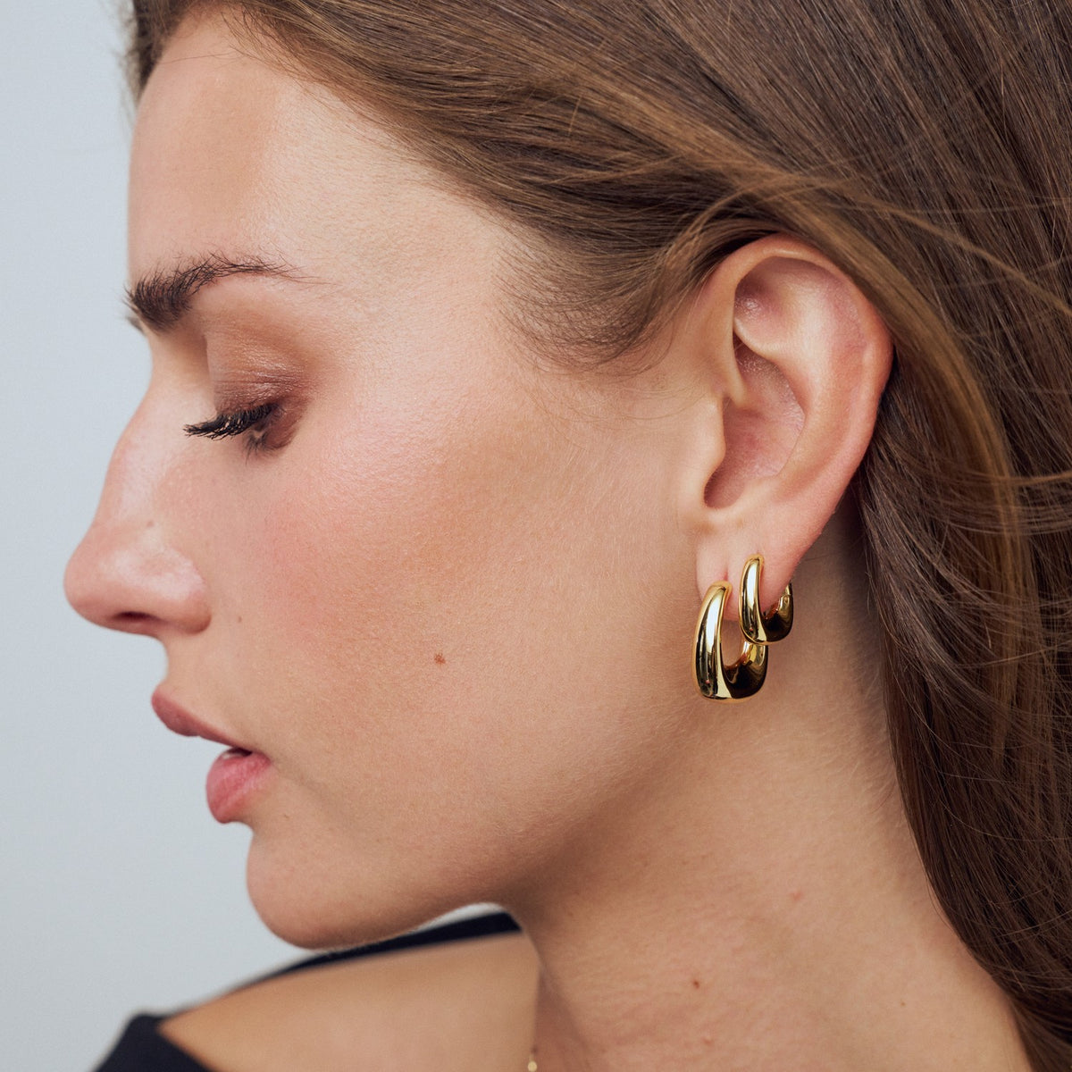 Close-up of a woman wearing gold hoop earrings against a neutral background