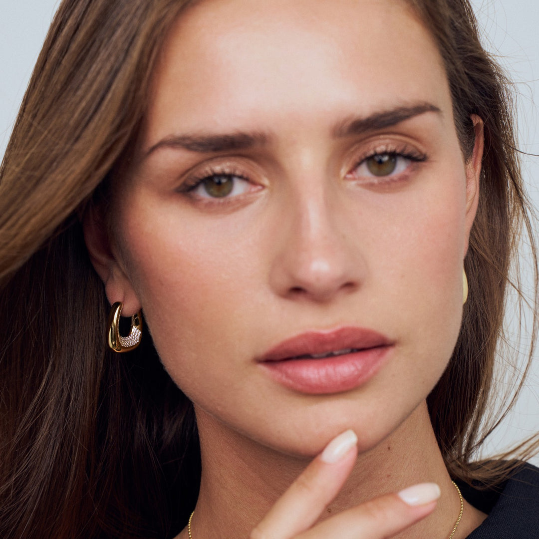 Close-up of a woman wearing gold hoop earrings with a neutral background