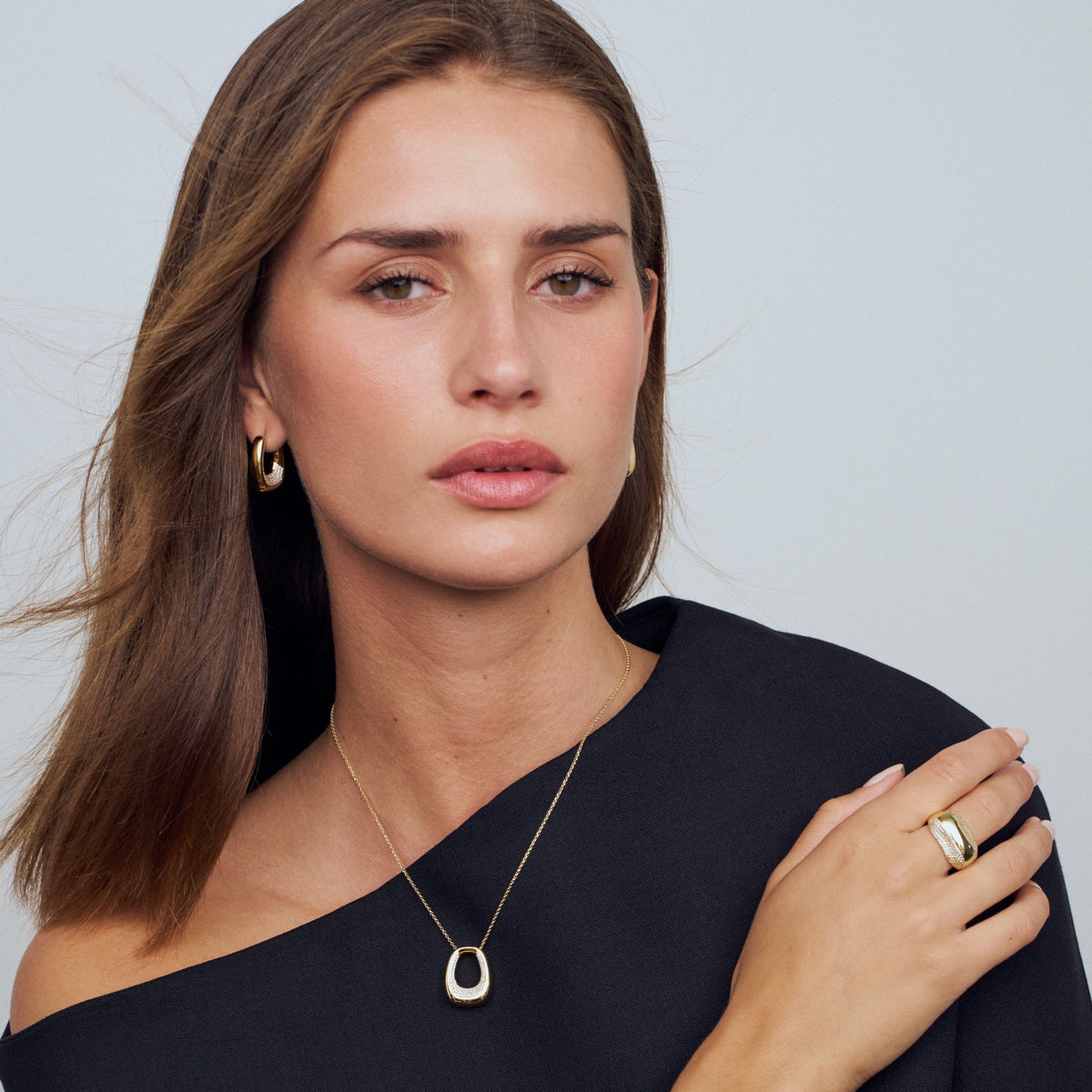 Woman wearing gold jewelry including earrings, necklace, and ring on a plain background