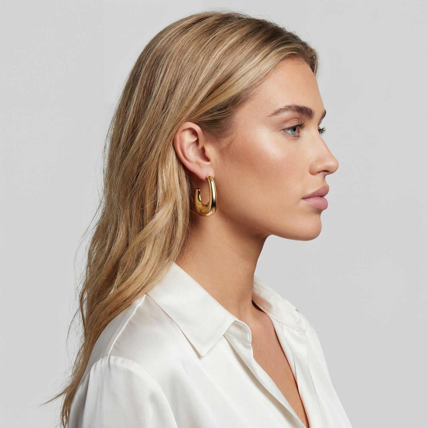 Woman wearing gold hoop earrings with a plain background