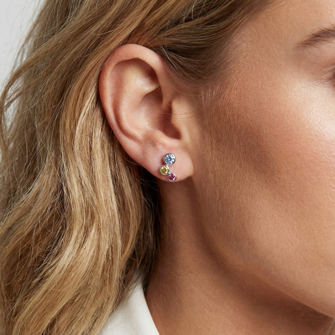 Close-up of a person wearing colorful stud earrings with blonde hair.