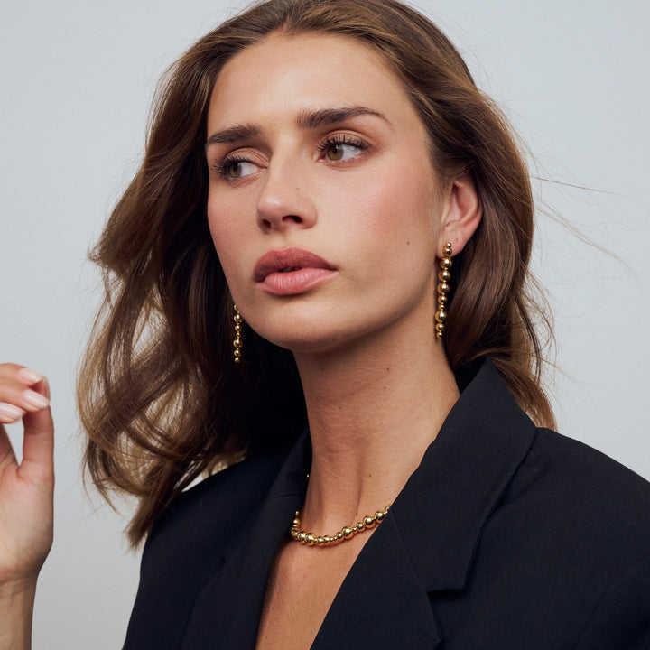 Woman wearing gold earrings and necklace against a neutral background