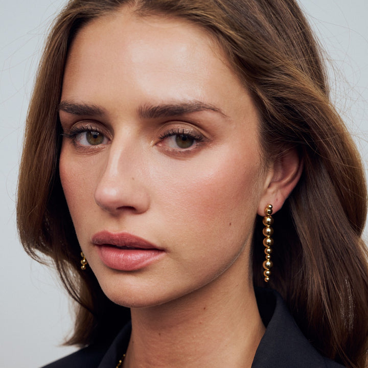 Close-up of a woman wearing gold earrings against a neutral background