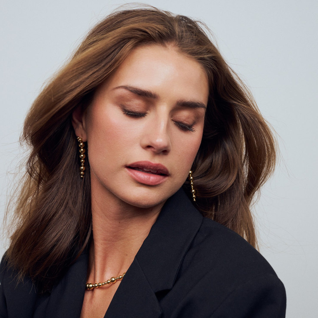 Woman wearing gold earrings and a necklace against a neutral background