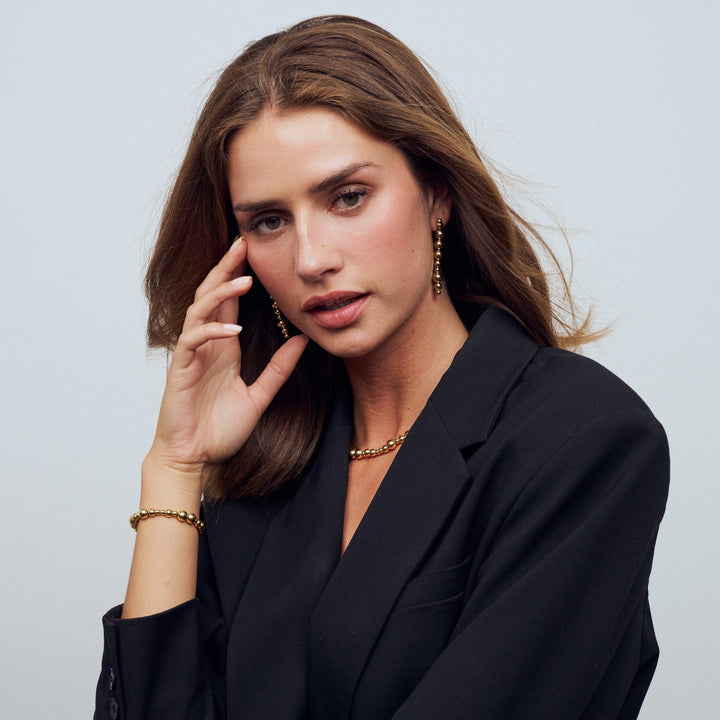 Woman wearing a black blazer with gold jewelry against a light gray background