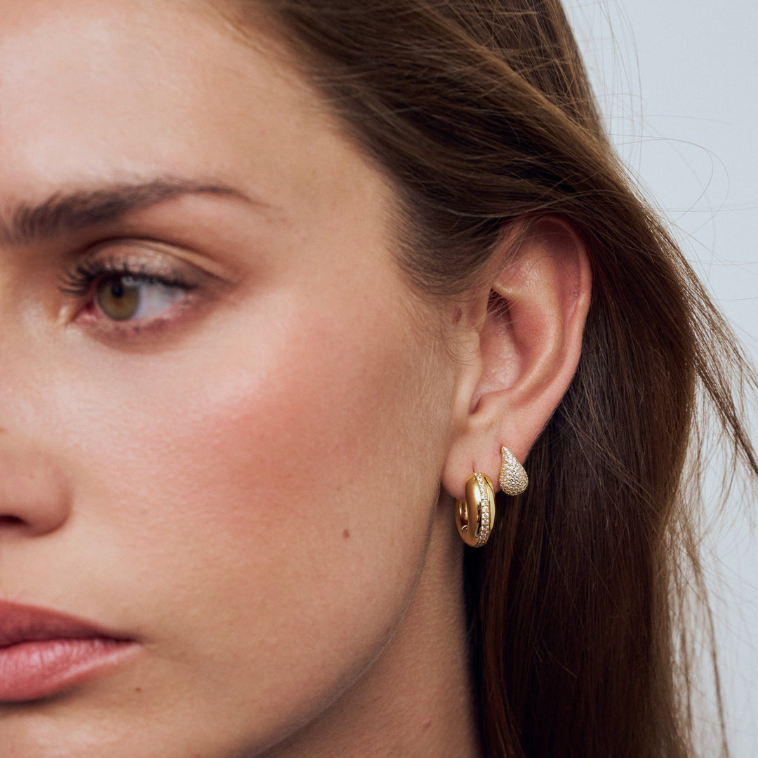 Close-up of a woman wearing gold hoop earrings with a neutral background