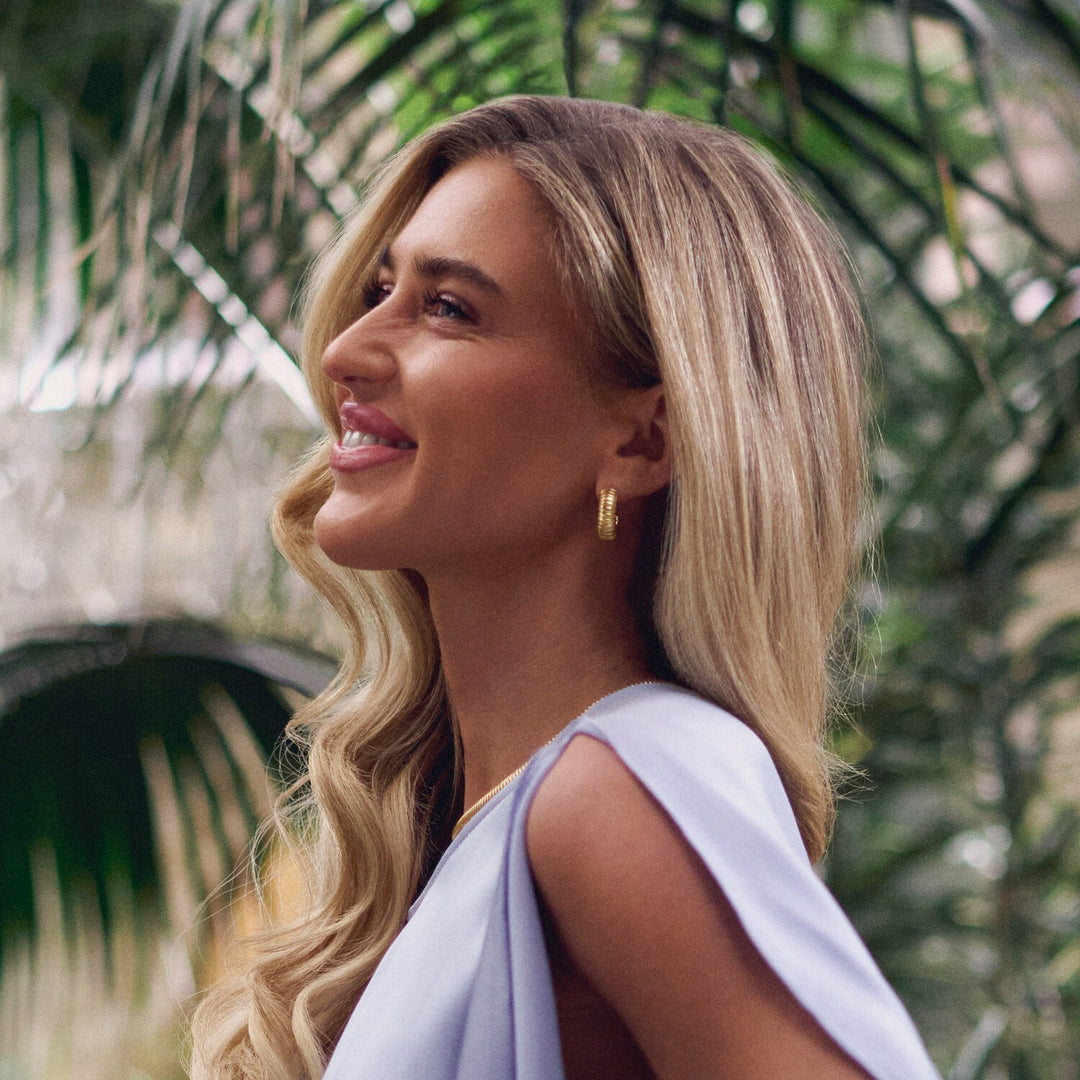 Woman with blonde hair and a light blue top standing among green foliage.
