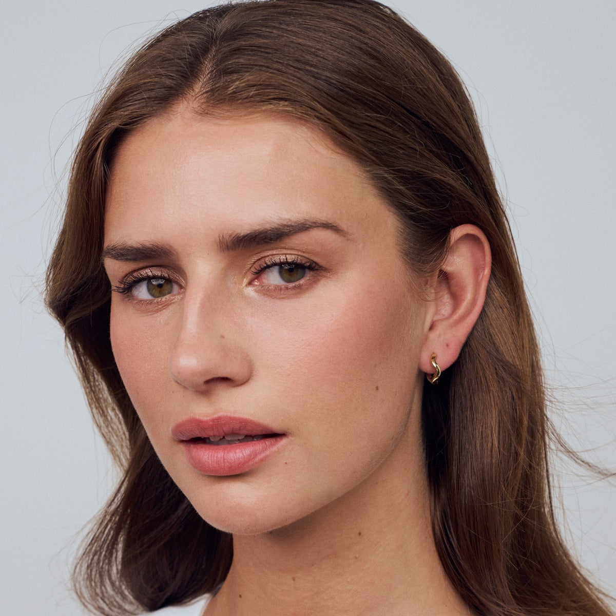 Close-up of a woman with long brown hair and a neutral expression on a light gray background
