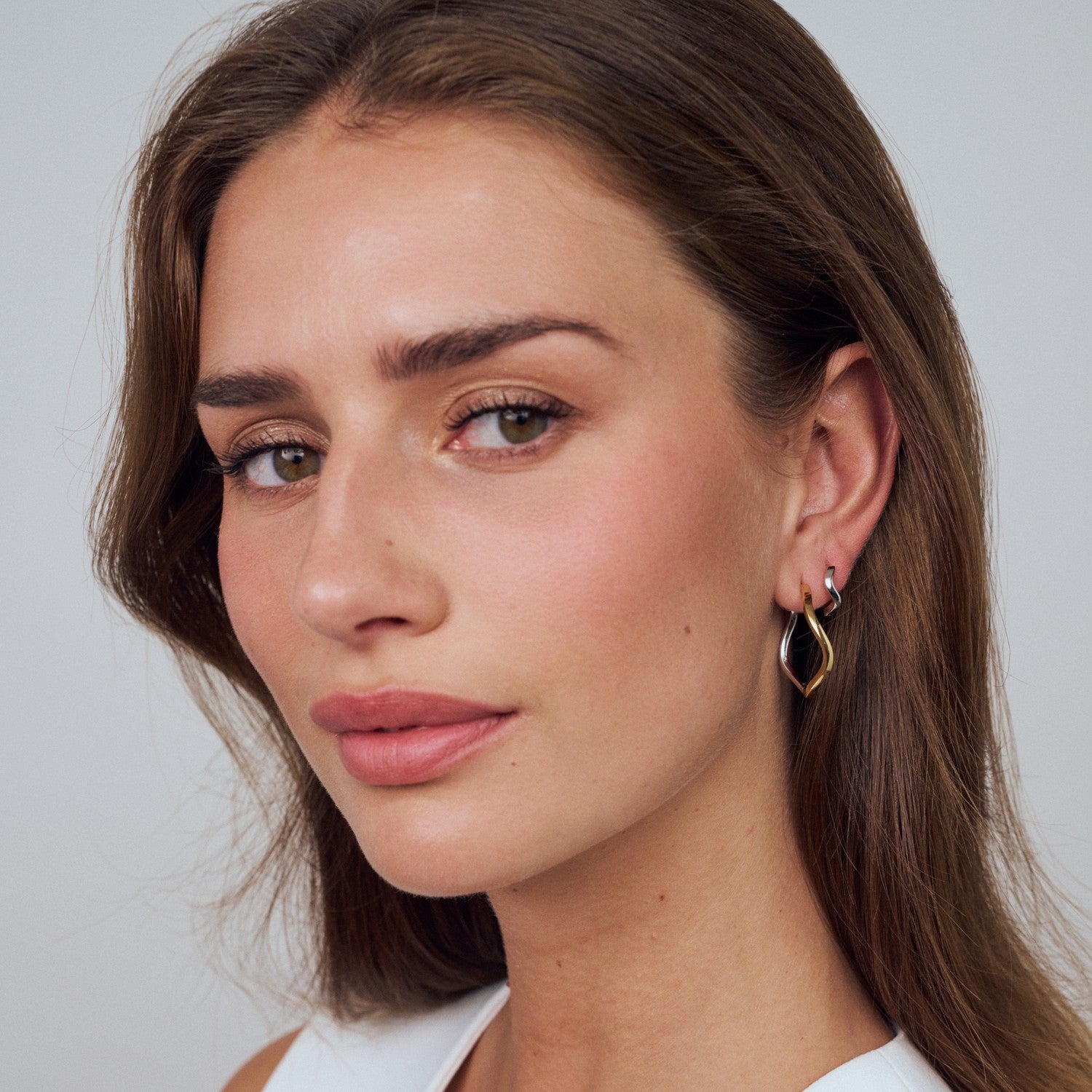 Close-up of a woman wearing gold hoop earrings against a neutral background