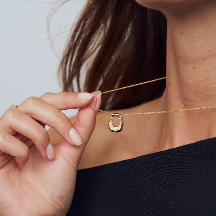 Gold necklace with a unique pendant being worn and adjusted by a person.