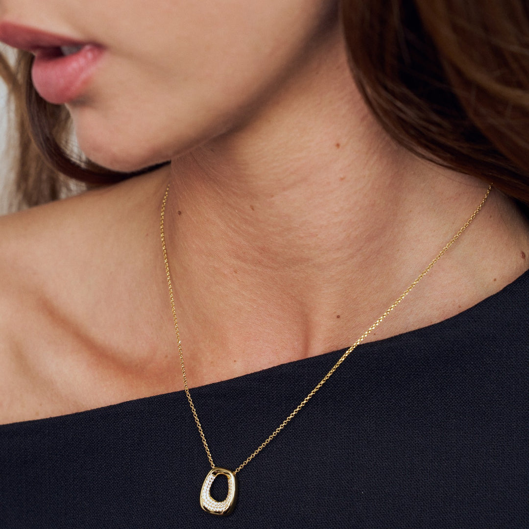Close-up of a gold necklace with a pendant on a person wearing a black top.
