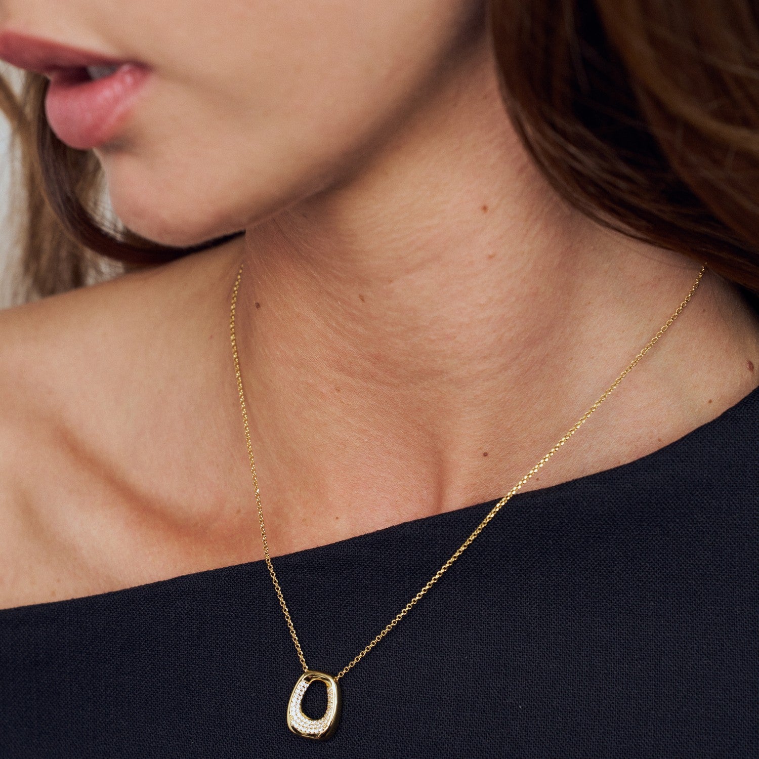 Close-up of a gold necklace with a pendant on a person wearing a black top.
