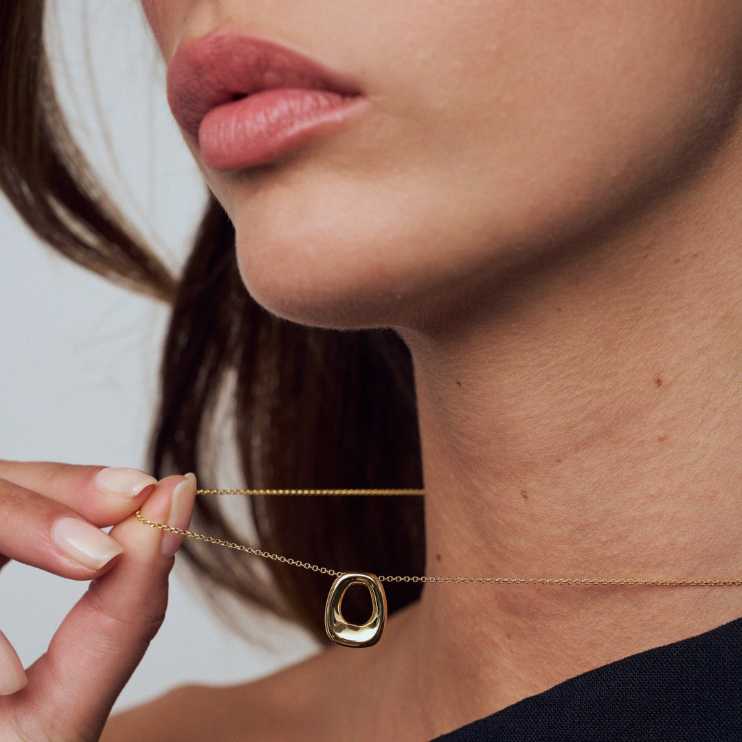 Close-up of a person wearing a gold necklace with a small pendant.
