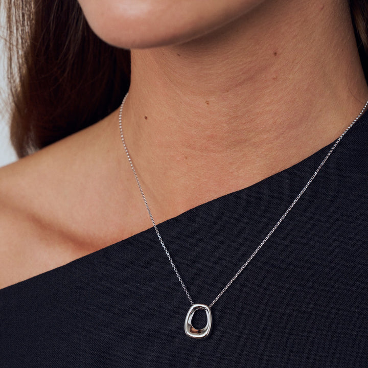 Silver necklace with a unique pendant worn by a person against a neutral background