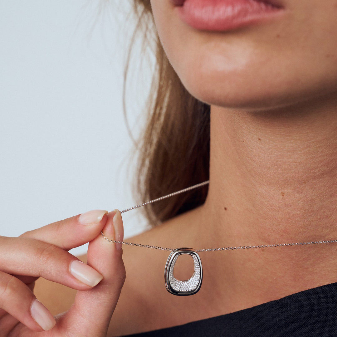Necklace with a pendant being held by a hand against a neutral background