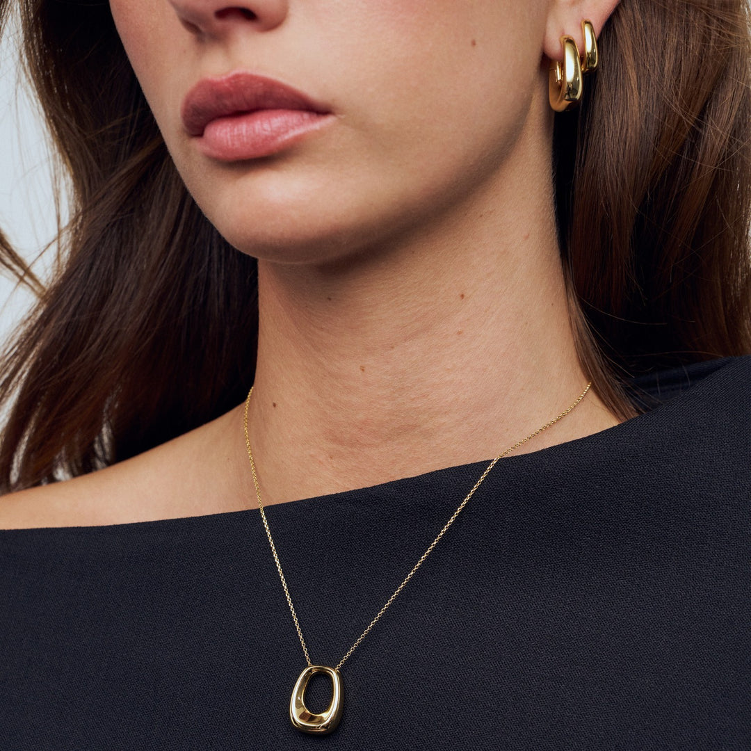 Close-up of a person wearing a gold necklace and earrings on a black background