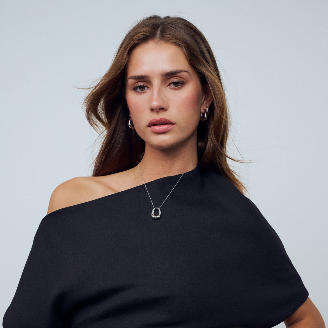 Woman wearing a black off-shoulder top and a necklace with a pendant against a light gray background
